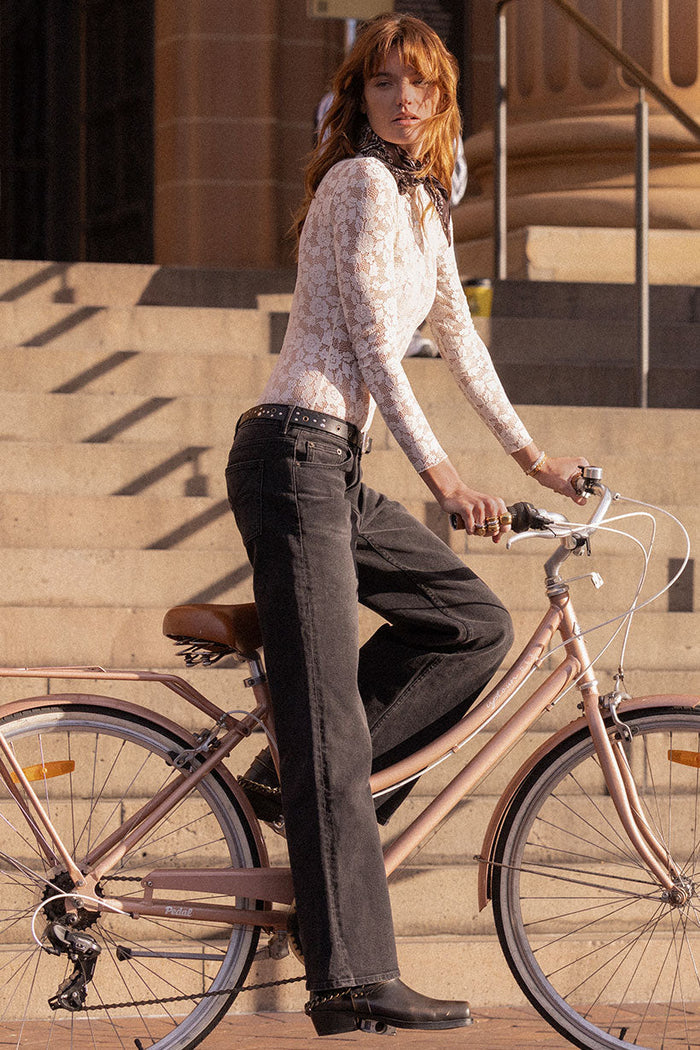 Model side-on astride a bicycle, vintage black relaxed-fit organic cotton jeans with mid rise and 5-pocket design