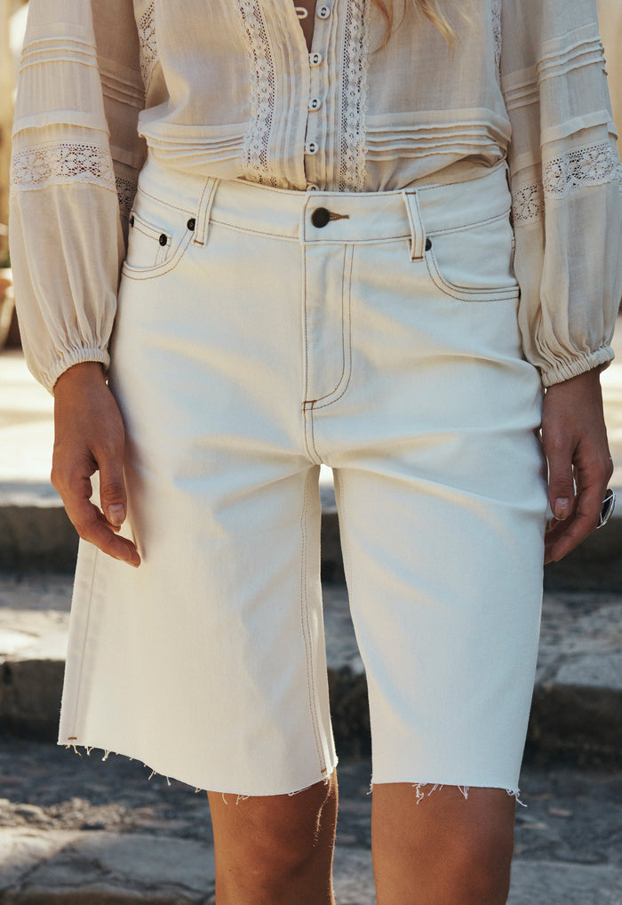 Front view of a model wearing Salt organic cotton denim shorts, raw hem edge, contrast stitching, mid rise fit