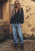 Model front-on in washed indigo baggy jeans, mid-rise relaxed leg, styled with black blouse and brown boots