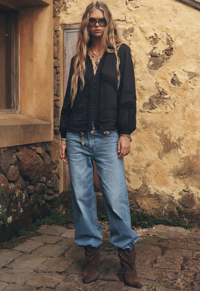 Model front-on in washed indigo baggy jeans, mid-rise relaxed leg, styled with black blouse and brown boots