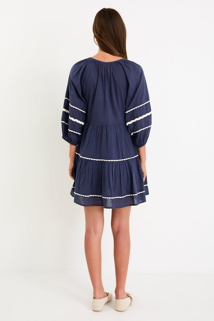 Model wearing a navy tiered short sleeve smock dress with a relaxed fit and contrast trim detail.
