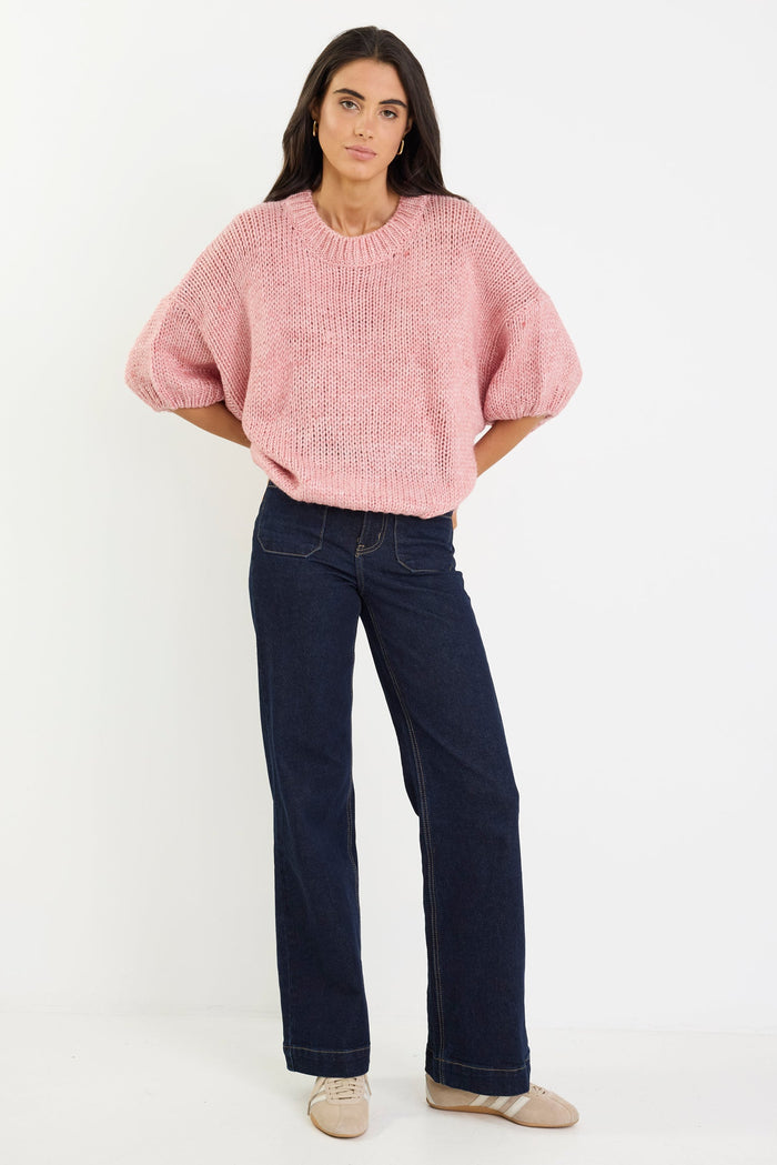 Woman wearing a pink sweater and dark blue jeans on a white background