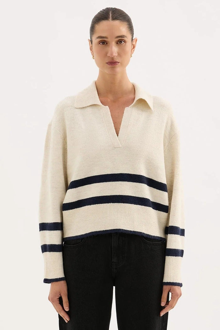 Woman wearing a cream sweater with navy stripes and black pants on a white background