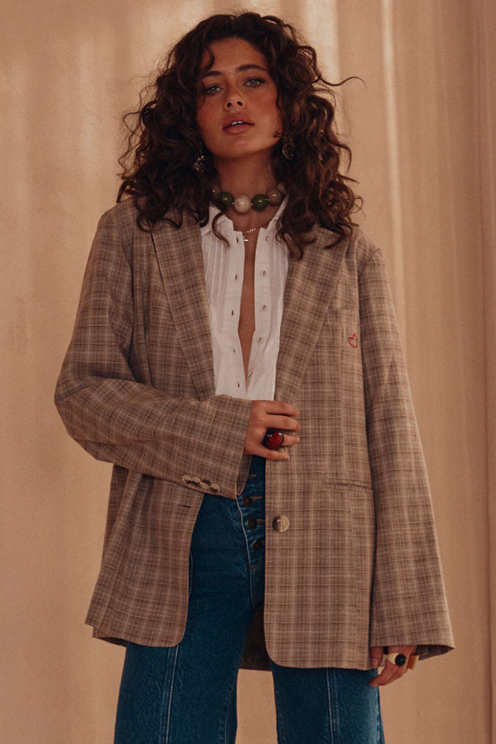 Front view of oversized check blazer with embroidered heart detail on chest pocket, styled over white shirt with jeans