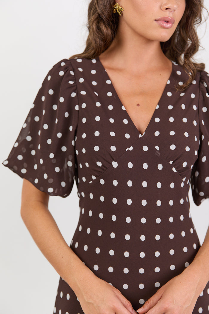 Woman wearing a brown dress with white polka dots against a plain background