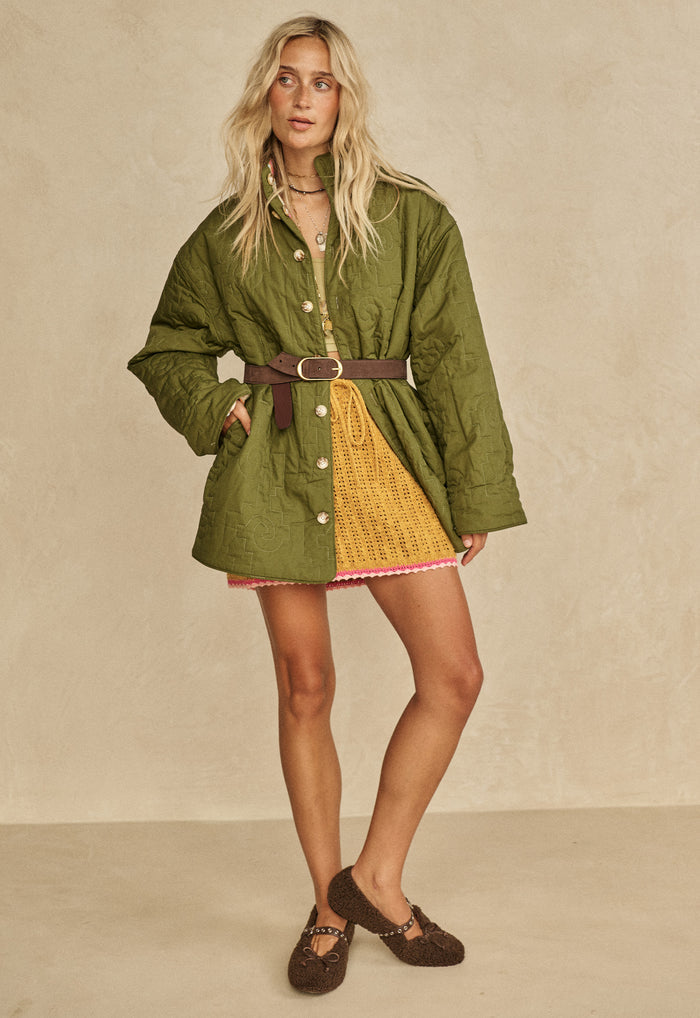 Model wearing Coastal Granny Mini Skirt in Mustard knit, styled under green quilted jacket with brown belt
