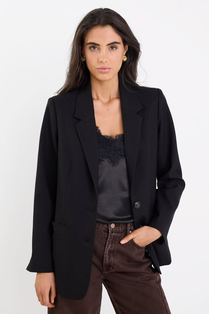Woman wearing a black blazer over a black top with brown pants on a white background