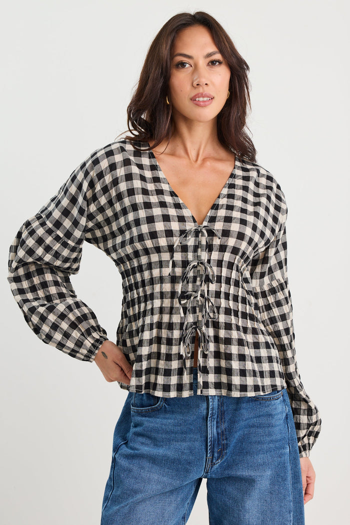 Woman wearing a black and white checkered blouse with blue jeans on a white background