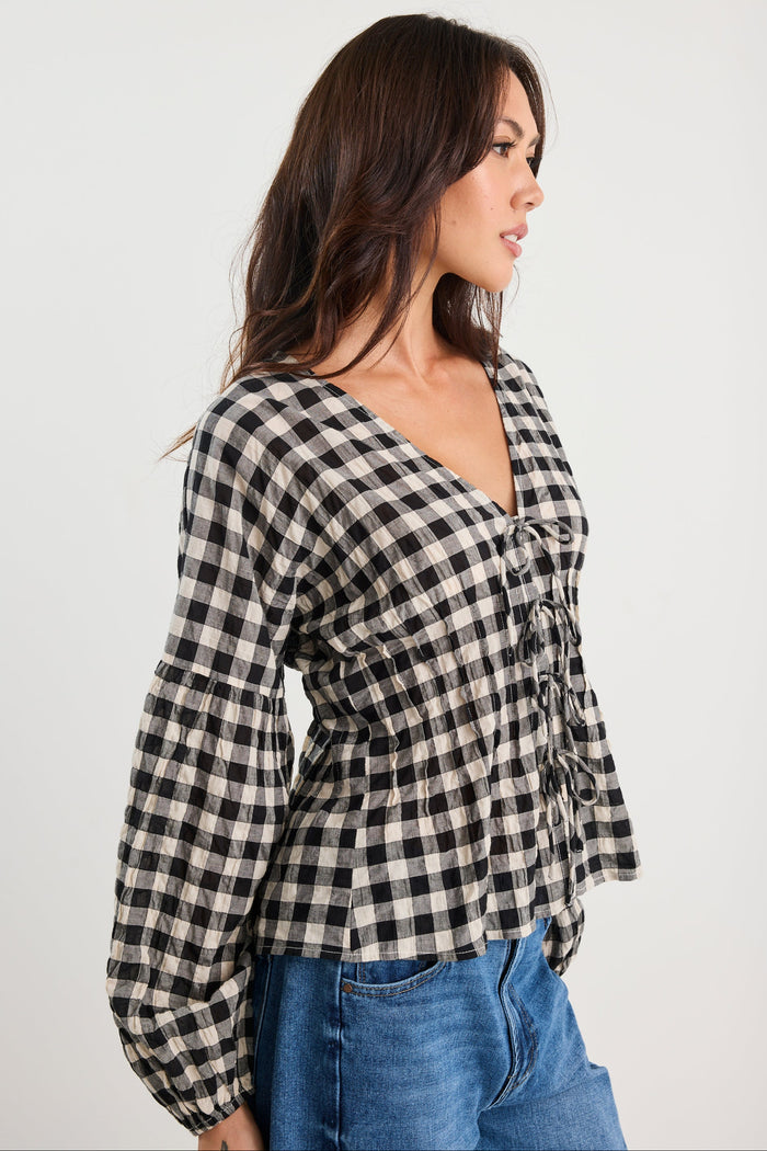 Woman wearing a black and white checkered blouse with blue jeans on a white background