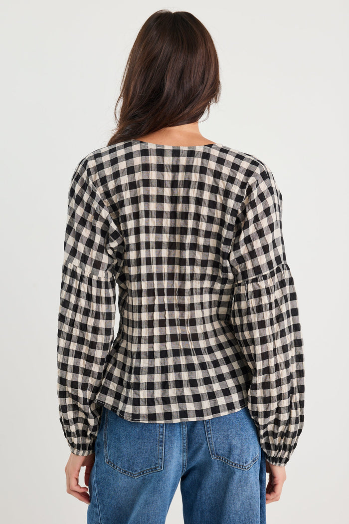Person wearing a black and white checkered shirt and blue jeans on a plain background