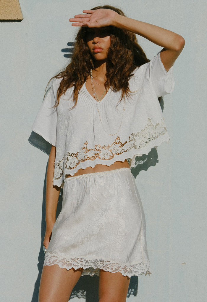 Dubois Bias Mini Skirt in Pearl flat lay, white Naia acetate with floral lace hem trim, front view
