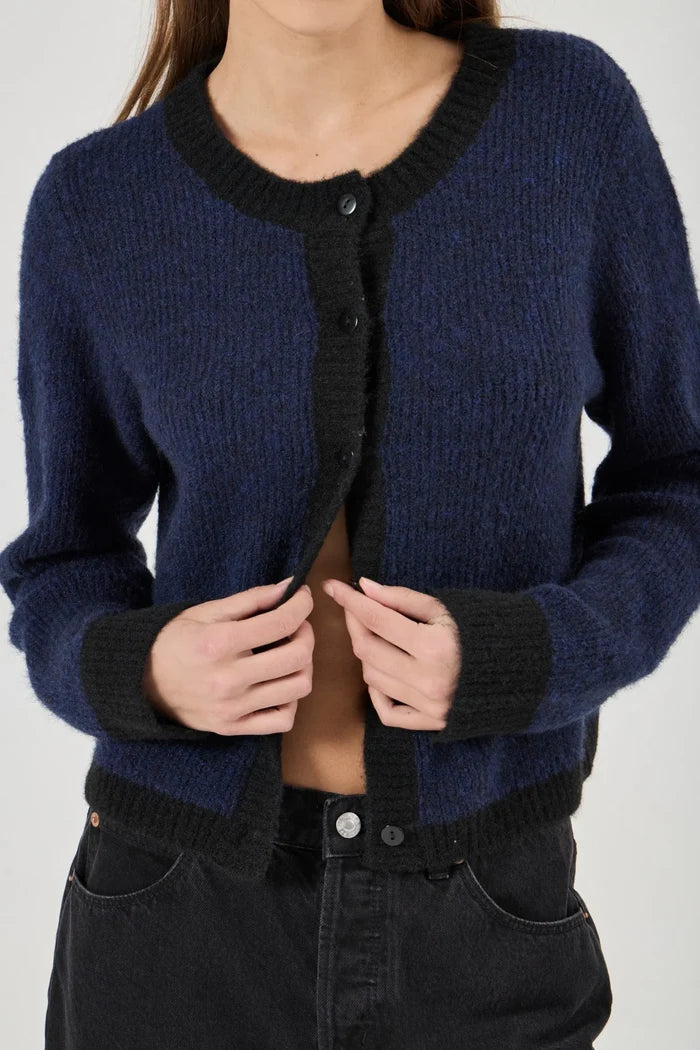 Person wearing a navy blue cardigan with black trim on a plain background