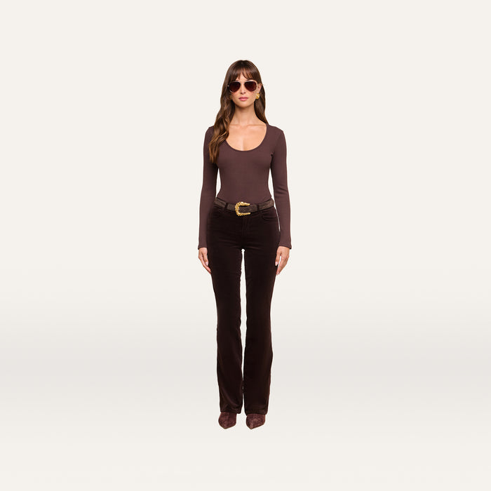 A woman stands against a plain white background, wearing sunglasses, the Elara Scoopneck Bodysuit—a long-sleeve brown stretch cotton modal piece that offers a body-contouring fit—paired with flared dark brown pants, a wide belt, and brown shoes.