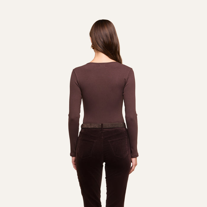 A woman with long brown hair, seen from behind, wears the Elara Scoopneck Bodysuit in a body-contouring fit along with dark brown pants against a plain off-white background.