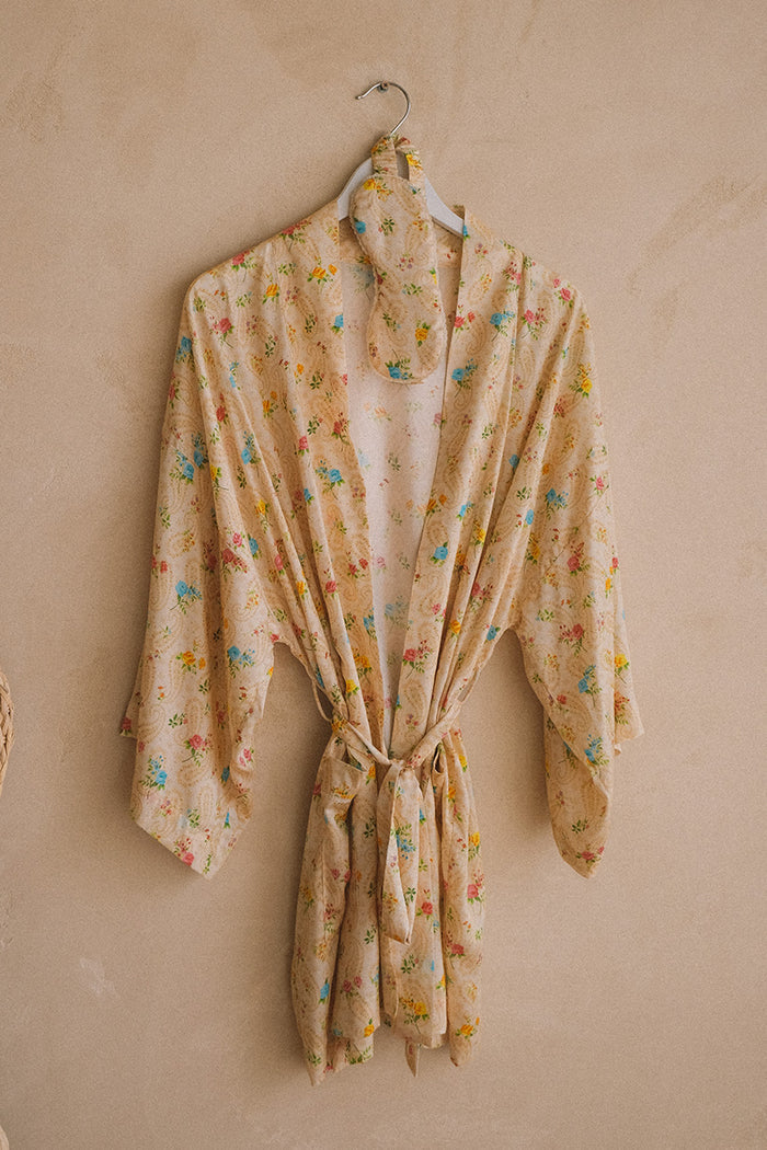 Floral robe and eye mask set hung on wall, belted at waist, multicolor ditsy print on cream ground