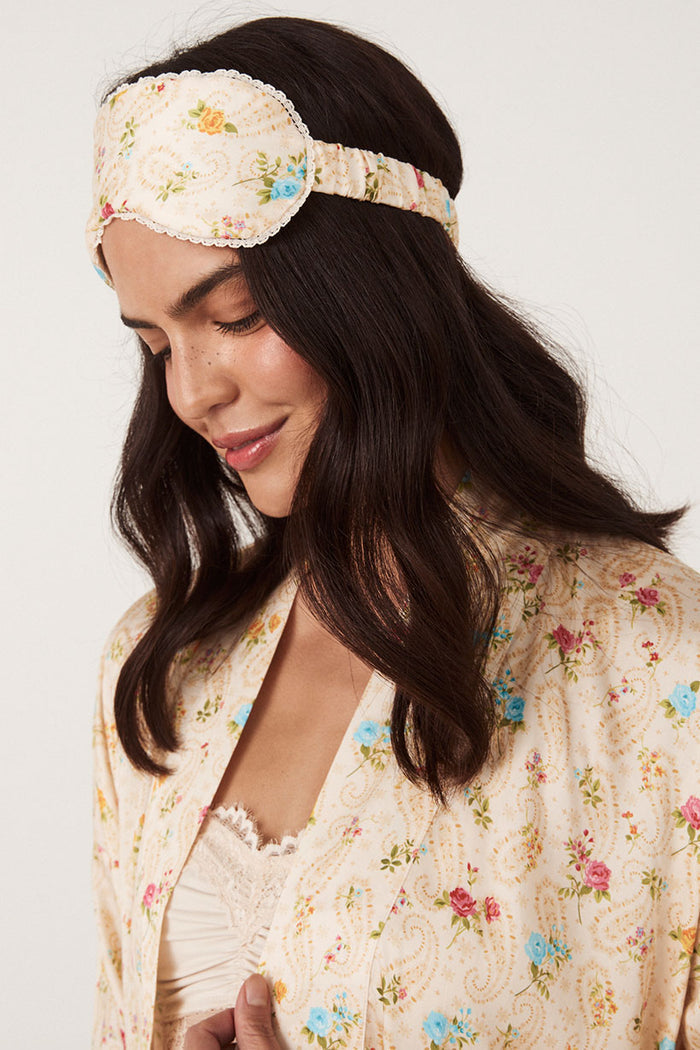 Close-up of floral eye mask with lace trim worn over forehead, paired with matching macaroon robe