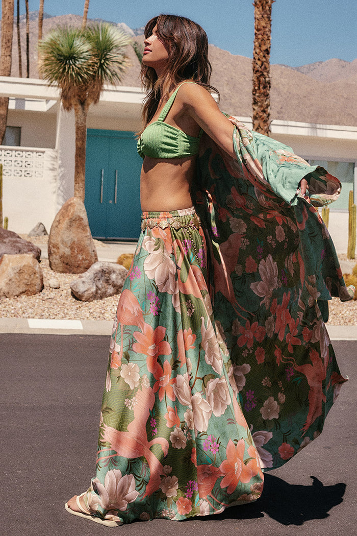 Side view of Floridian Maxi Skirt in Sage, floral print, elastic waist, floor-length, styled with green crop top outdoors
