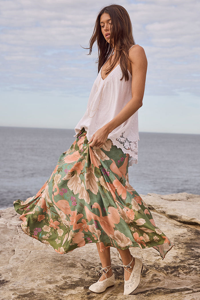 Side-front view of Floridian Maxi Skirt in Sage, floral flamingo print swirling on coastal rocks