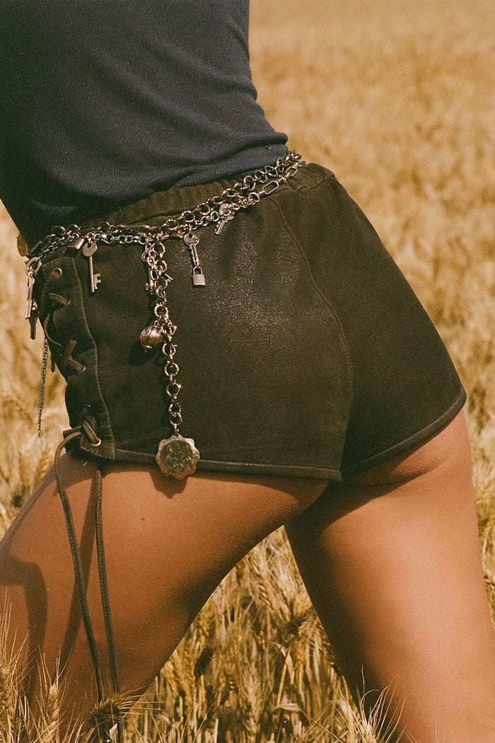 Side view of vintage brown leather mini short showing lace-up side detail and elastic waist, wheat field backdrop
