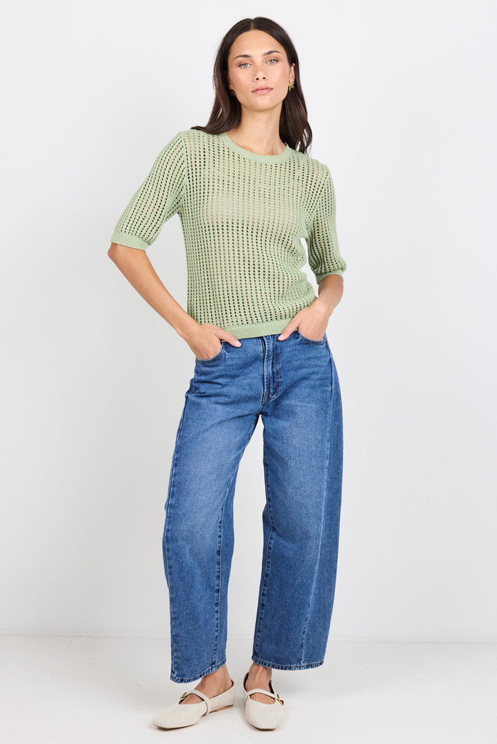 Woman wearing green knit tee and blue denim jeans on white background.