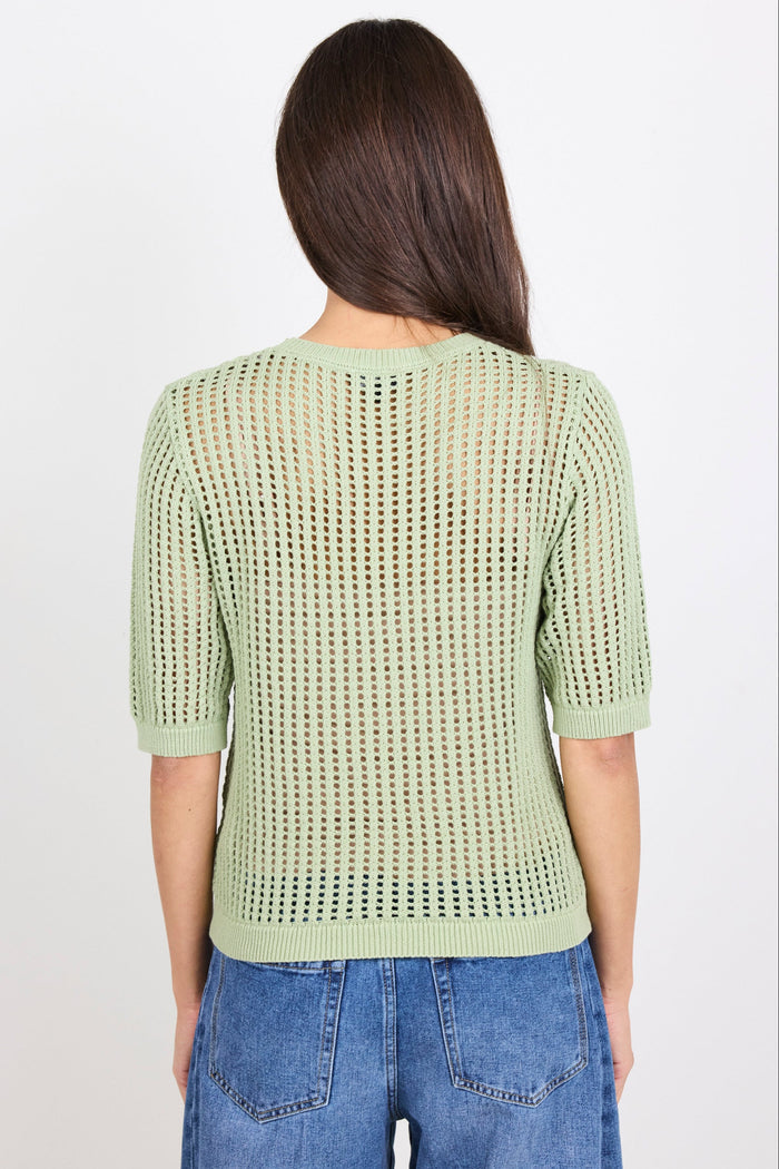 Woman wearing green knit tee and blue denim jeans on white background.
