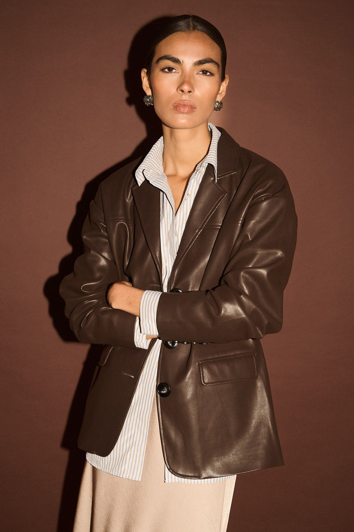 Woman wearing a brown leather jacket over a white shirt with a brown background
