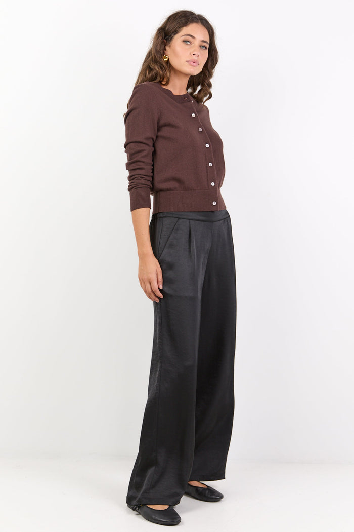 Woman wearing a brown button-up shirt and black wide-leg pants on a white background