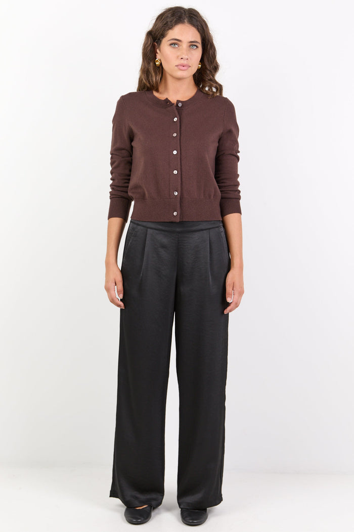Woman wearing a brown cardigan and black pants on a white background