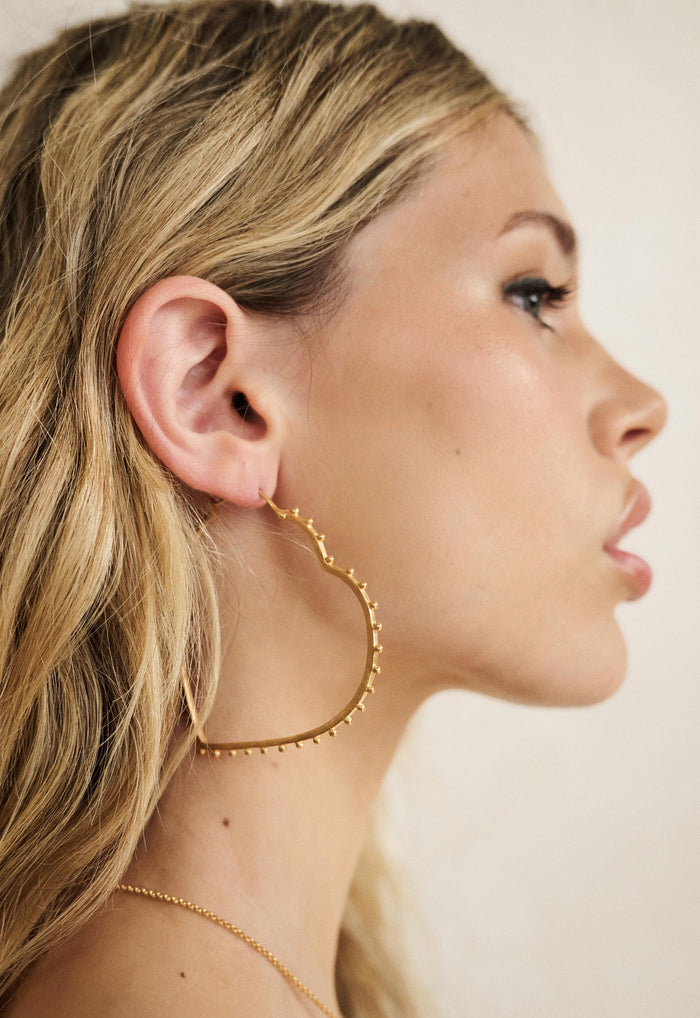 Side profile view of gold 22K-plated brass heart hoop earring with studded edge detailing, clip clasp fastening