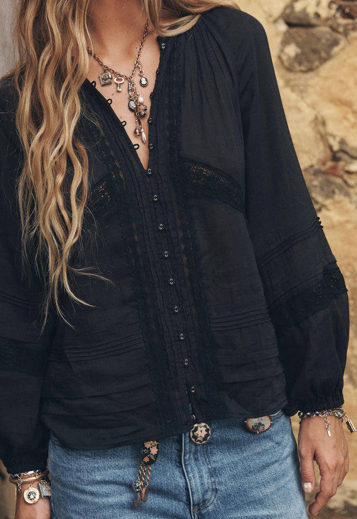Front-facing close-up of black blouse showing lace trim panels, pintuck detail, and front button opening with eyelet trim