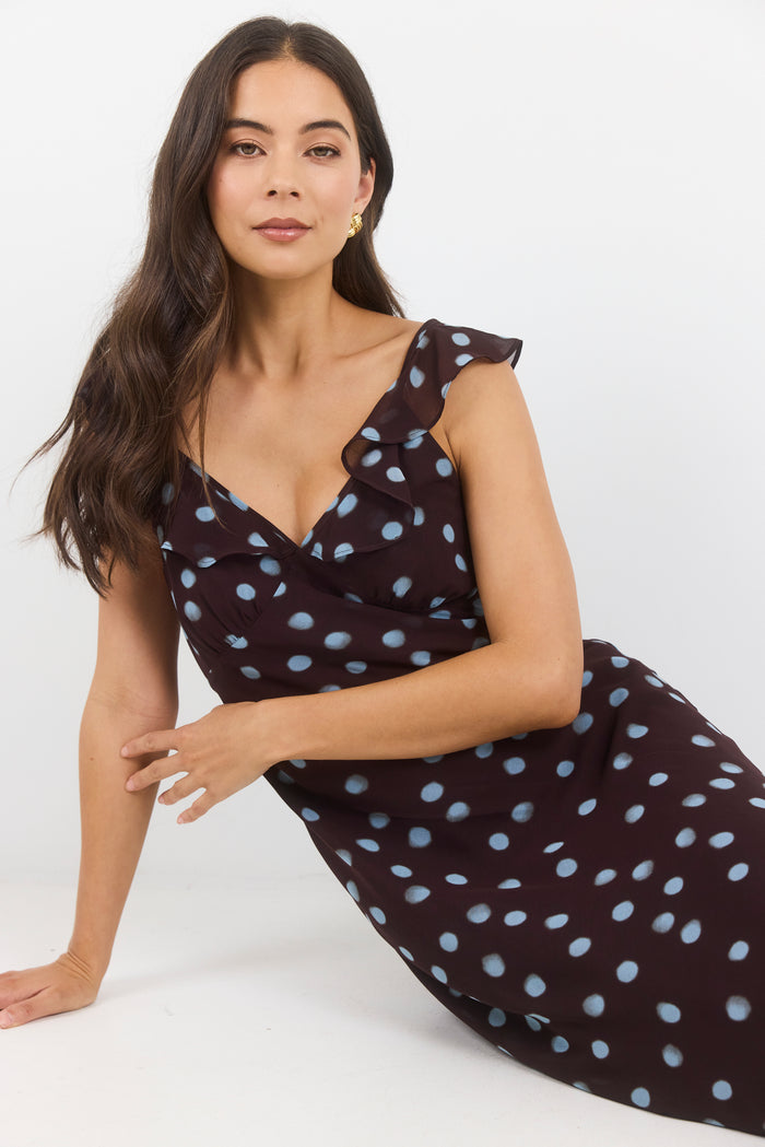 A woman wearing a dark brown wrap-style dress with light blue polka dots, posed on a clean white studio background.