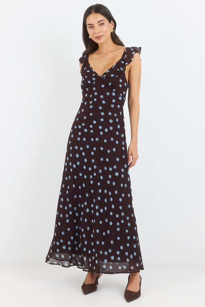 A woman modeling a sleeveless black maxi dress with a white and light blue polka dot pattern, ruffled shoulder straps, and a V-neckline, set against a plain white studio background.
col_pattern