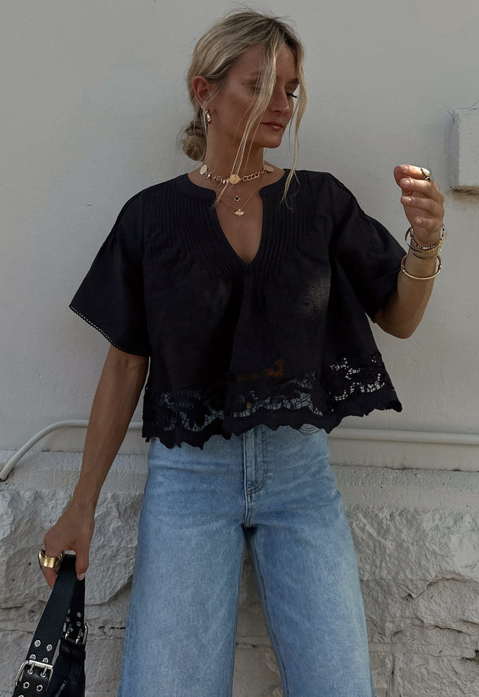 Front view of Kala Short Sleeve Blouse, black lace hem embroidery and pintuck detail, styled with light-wash jeans