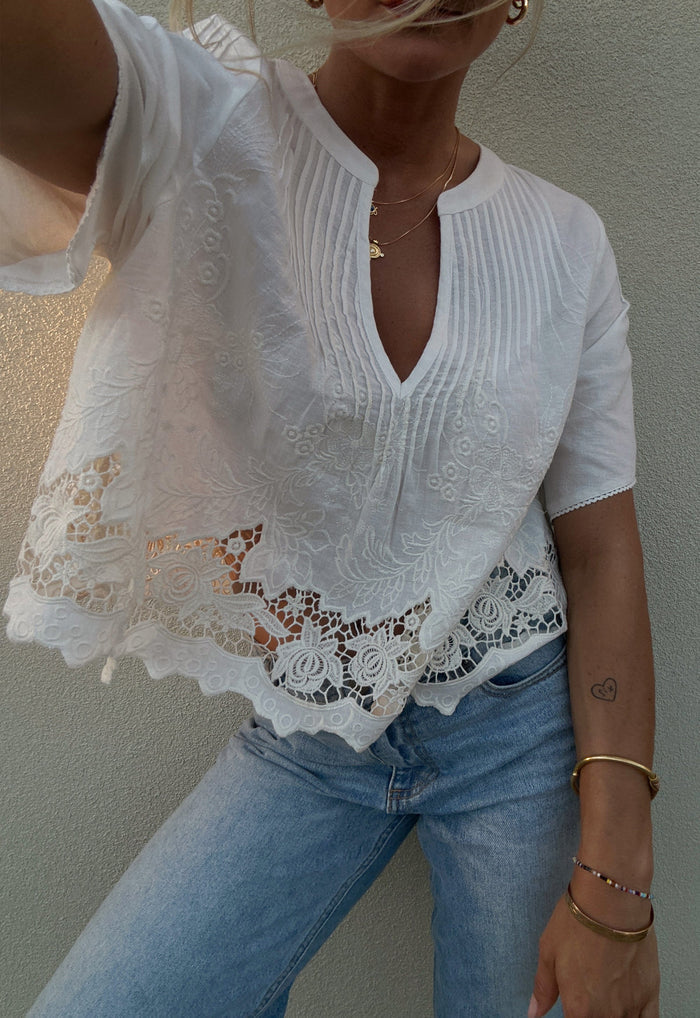 Front detail of pintuck V-neck blouse with floral lace hem and embroidery, styled with light-wash jeans