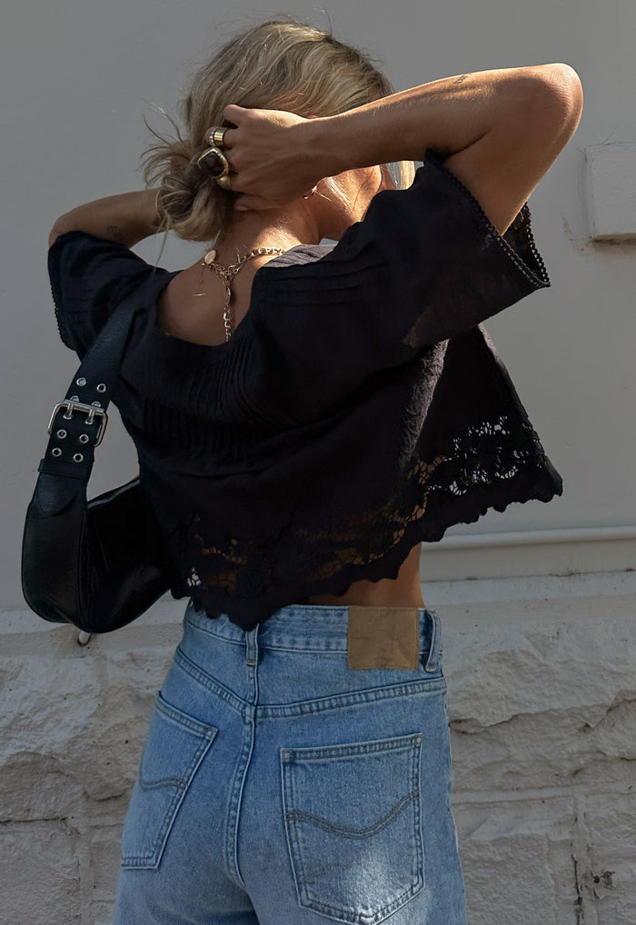 Back view of black organic cotton linen blouse with lace-trim hem and flutter sleeves, styled with blue jeans
