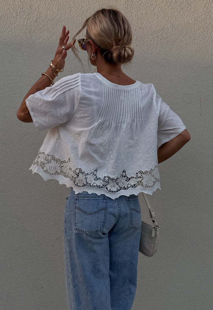 Back view showing pintuck detail and floral lace hem trim on white organic cotton-linen cropped blouse