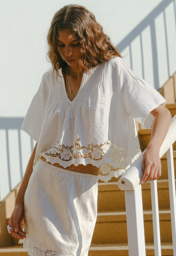 Front view of crochet lace hem detail on white organic cotton-linen cropped blouse with pintuck body on stairs