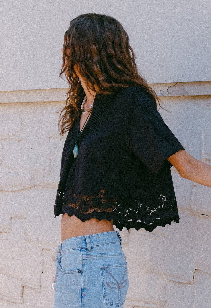 Side view of black organic cotton linen crop blouse with lace hem, scalloped edge, and pintuck detail on body