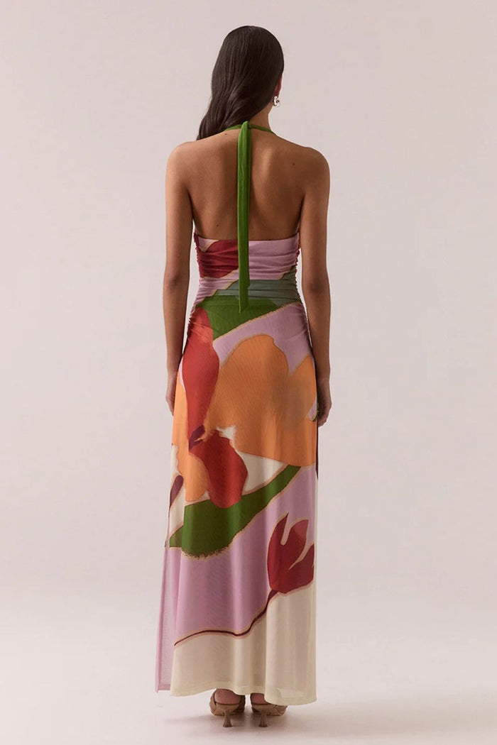 Woman wearing a colorful floral dress with a green strap on a plain background
