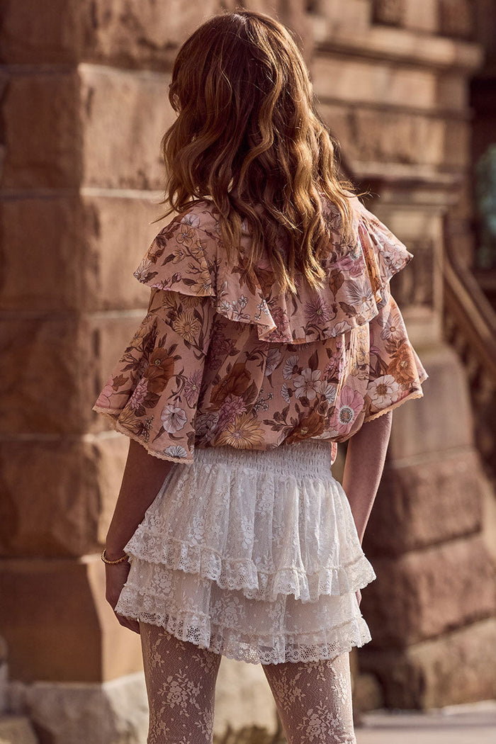Back view of a model wearing cream layered lace mini skirt with shirred waist, styled with floral top