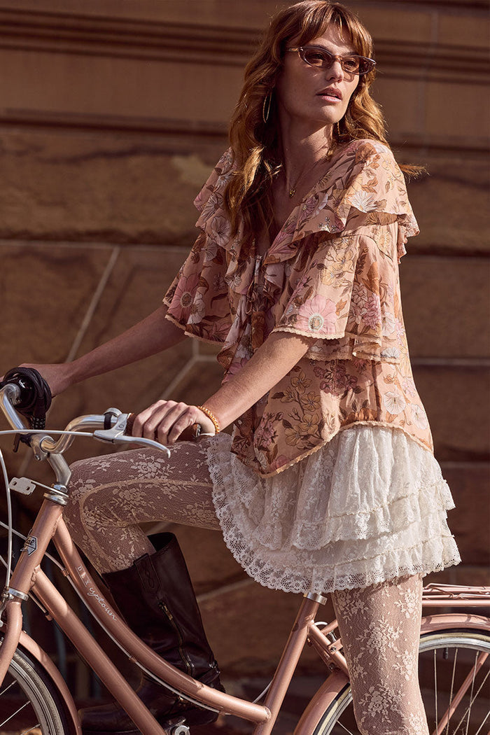 Model styled with floral top beside a bicycle, cream lace mini skirt with layered lace hem trim and shirred waist visible