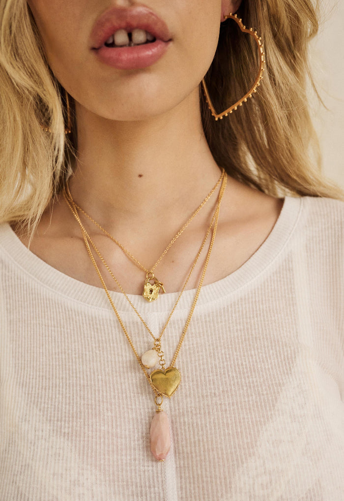 Close-up of layered gold necklaces with padlock charm and Lolita pink opal stone pendant on gold chain