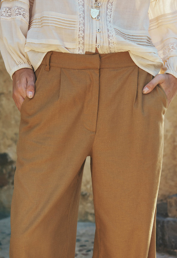 Close front view of tan hemp-blend wide-leg pants showing front pleats and side pockets, hands in pockets
