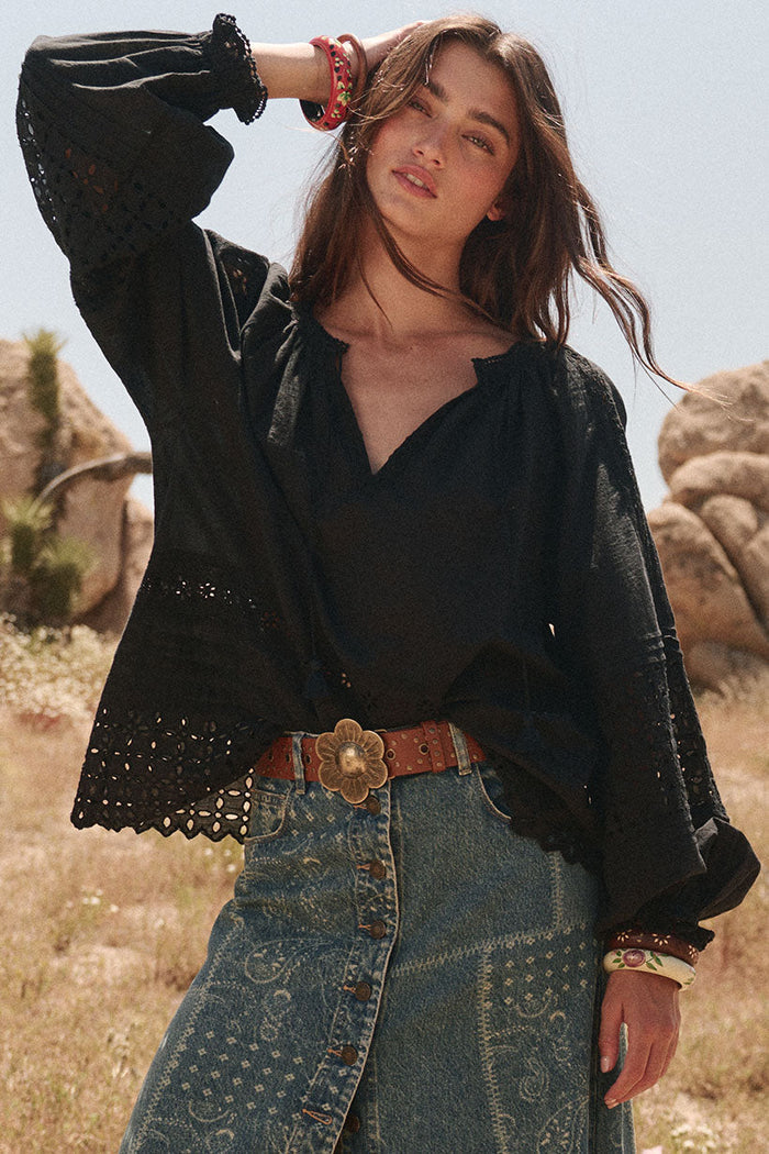 Front view of black Schiffli anglaise blouse with blouson sleeves, ball-trim cuffs, and centre-front tassel ties