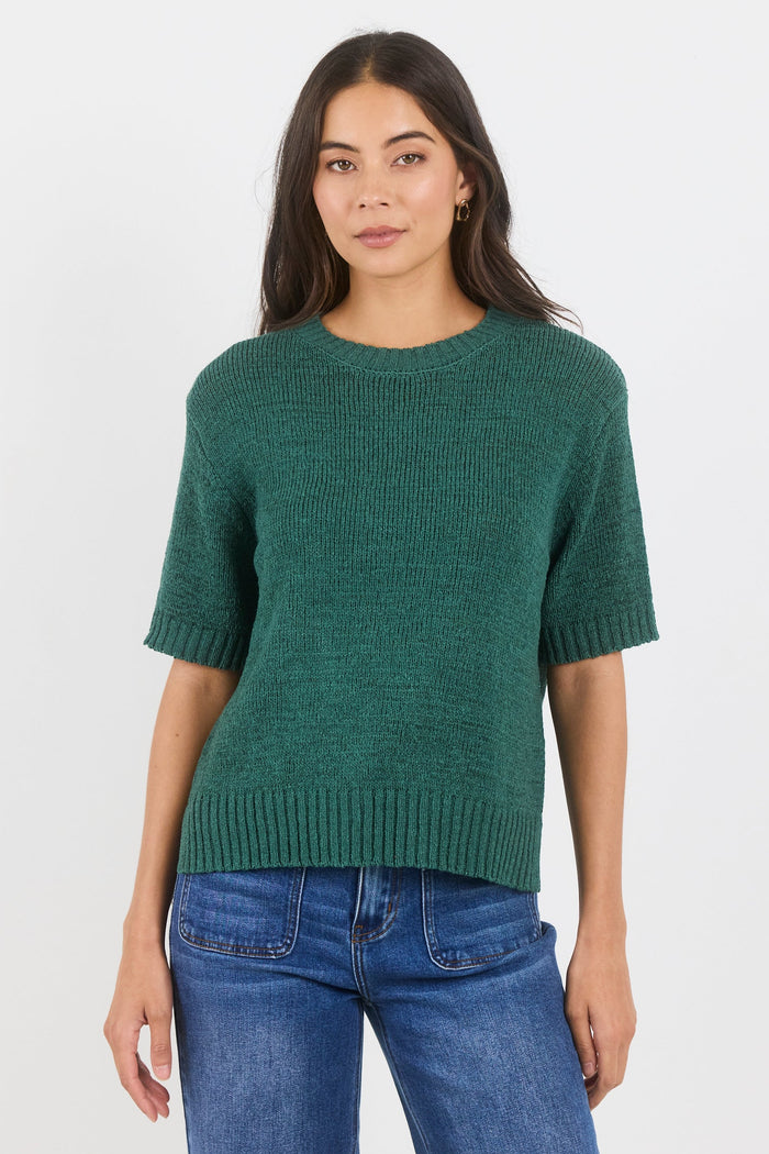 Woman wearing a green sweater and blue jeans on a white background