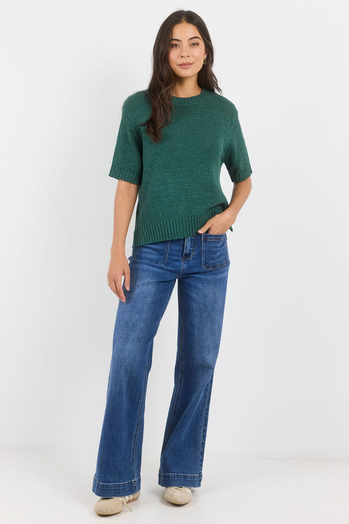 Woman wearing a green sweater and blue jeans on a white background