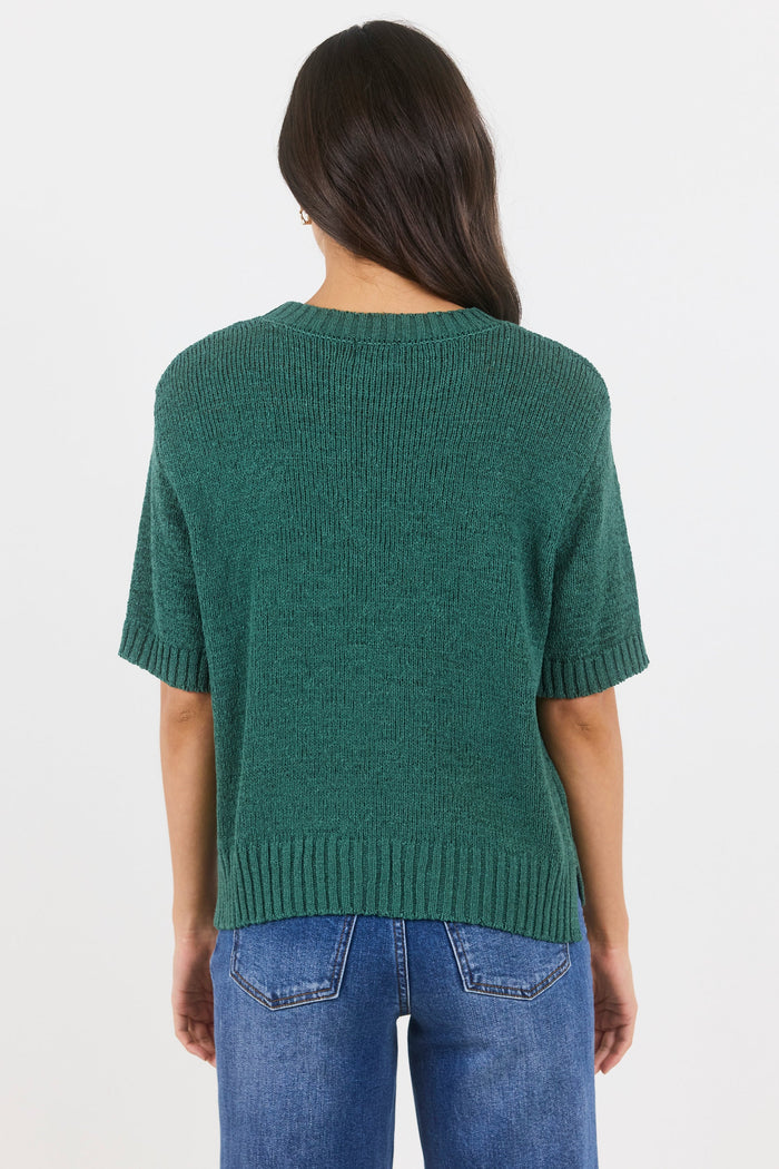 Person wearing a green knitted sweater and blue jeans on a white background