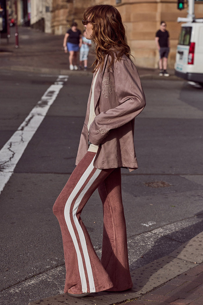 Model side view wearing chocolate terry flares with cream contrast side stripes and flared leg on city street