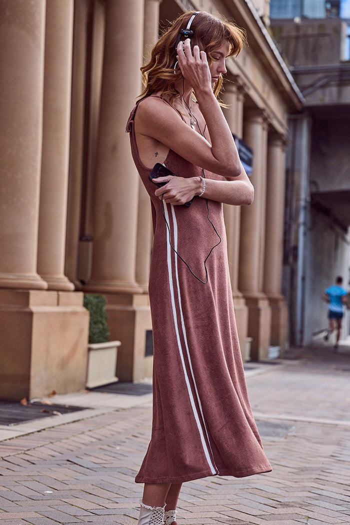 Side profile of a model in chocolate terry maxi dress, contrast white side stripes and tie shoulder detail visible