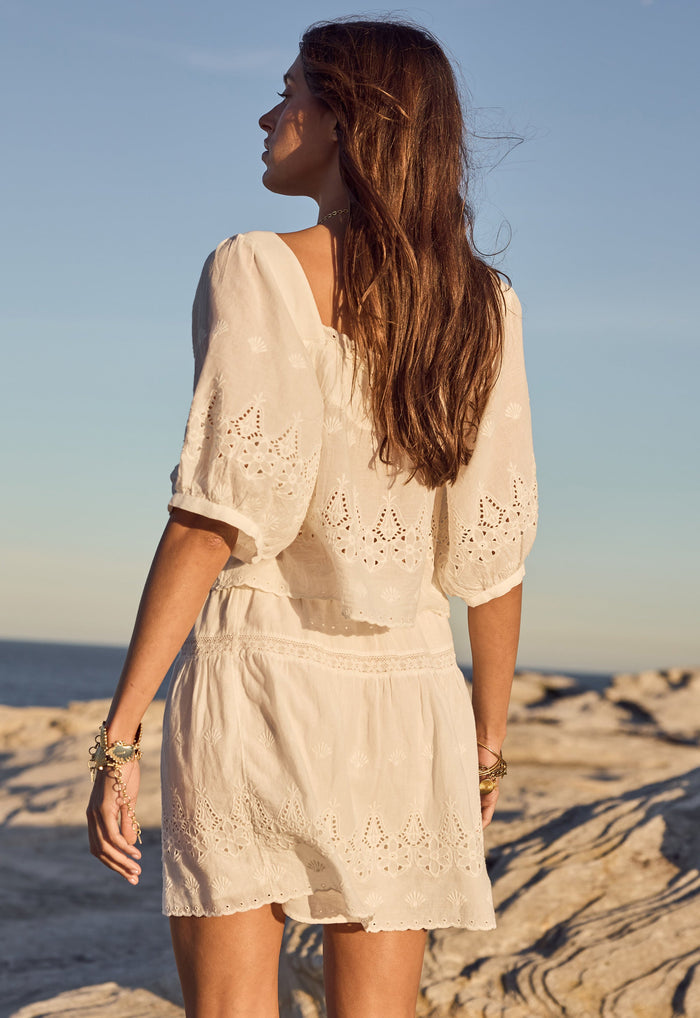 Back view of eyelet anglaise mini skirt with inserted lace trim and scallop hem, styled on rocks at golden hour